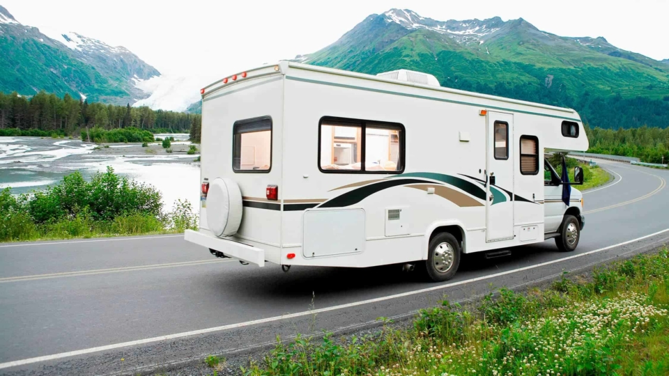 RV driving around a lake with a glacier in the distance